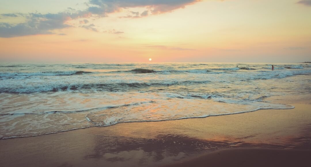 Atardecer en la playa con cielo colorido, olas suaves y reflejos dorados en la arena mojada.